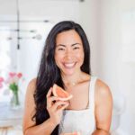 Woman in kitching smiling eating grapefruit